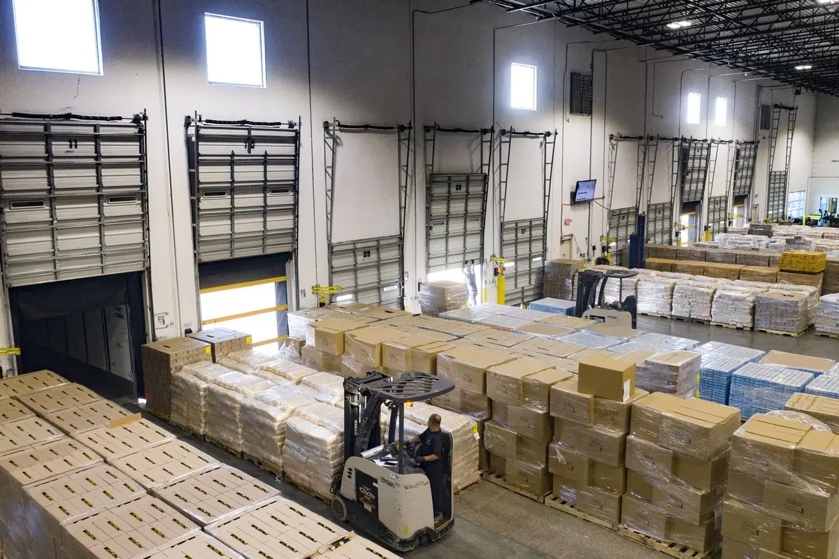 A forklift driver moves among pallets of boxed goods beside loading dock doors in a distribution warehouse in Houston, Texas.