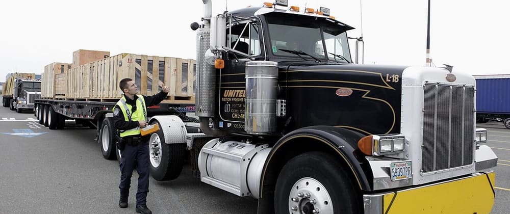 An officer in a safety vest signals a flatbed truck through an inspection station in Seattle, Washington.