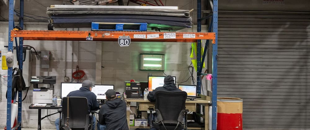 Three staff members work at computer desks set up under the storage racks of a food bank warehouse in central Pennsylvania.